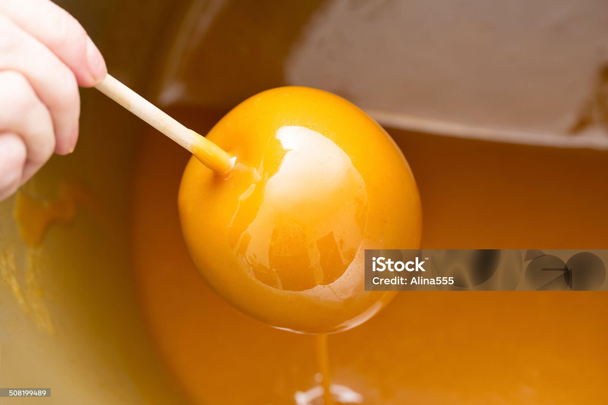 A toffee apple being made, the apple held by the stick dipped in the toffee sauce to cover it